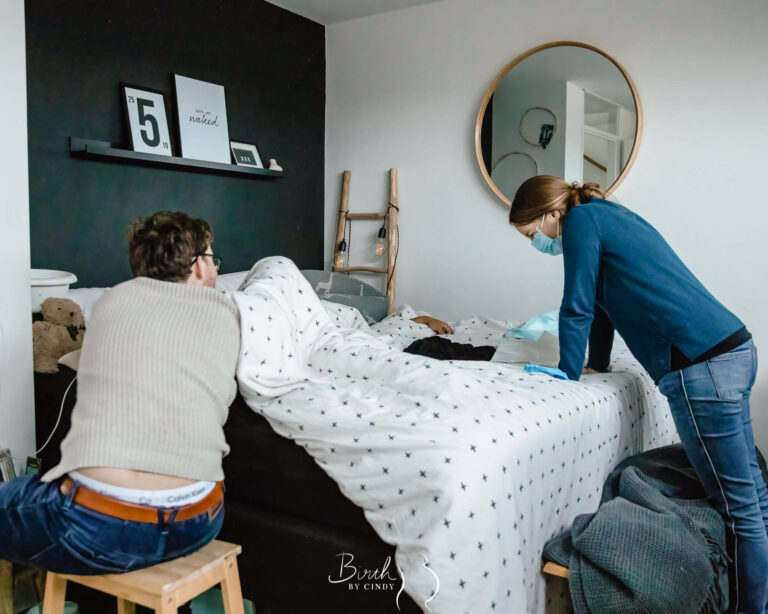 Vrouw met weeen thuisbevalling op bed met geboortefotograaf erbij in amersfoort
